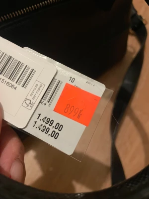 Svart handväska från Guess - Stilren svart handväska från Guess med både handtag och axelrem. Väskan har flera fack, ljusbeige innerfoder med Guess-logga och snygga guldfärgade metalldetaljer. Perfekt för dig som vill ha plats för allt viktigt och ändå se chic ut.