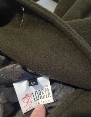 Mörkgrön kappa från Loreta Collection - Snygg mörkgrön kappa från Loreta Collection med bred krage och dekorativa knappar. Tillverkad i en lyxig mix av 70% kashmir, 15% angora och 15% polyamid. Perfekt för dig som vill ha en elegant och varm look under höst och vinter.