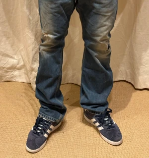 Adidas Gazelle sneakers marinblå mocka - Säljer ett par Adidas Gazelle sneakers i marinblå mocka med vita detaljer och klassiska tre ränder på sidan. Skorna har snörning, platt sula och rund tå. Adidas-logga på tungan och sidan, samt 'Gazelle' i guldtext. Perfekt för dig som gillar retrostil och streetwear.