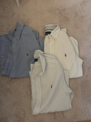 Ralph Lauren skjortor i bomull S - Tre snygga skjortor från Ralph Lauren i storlek S. En ljusblå med classic fit, två vita med custom fit och slim fit. Alla har den ikoniska broderade loggan på bröstet, klassisk krage och knappar framtill. Perfekt för dig som gillar stilrena och tidlösa plagg. 400kr/st