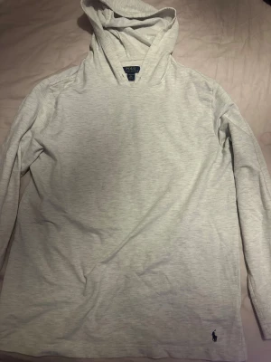 Ljusgrå hoodie från Polo Ralph Lauren - Snygg ljusgrå hoodie från Polo Ralph Lauren i storlek XL. Tröjan har huva, lång ärm och en diskret Polo-logga broderad nere vid höger sida. Tillverkad i mjuk bomull som är skön mot huden. Perfekt för chill dagar eller när du vill ha en clean look.
