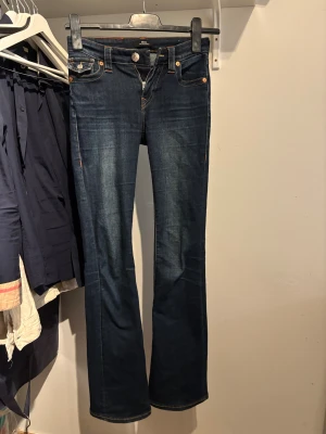 True Religion Becca Bootcut Jeans - Snygga mörkblå jeans från True Religion, modellen är  Becca Mid Rise Bootcut. I strl 24. perfekta för en trendig och avslappnad look. Skriv om du har frågor!