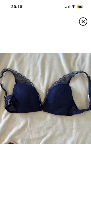 Marinblå spets bh - Snygg marinblå bh med spetsdetaljer längs kanterna. Bh:n har en feminin form och är axelbandslös, perfekt för att ge en chic vibe. Materialet är mjukt och stretchigt syntet med dekorativ spets som ger en extra touch.