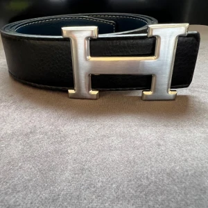 H-Bälte svart/marinblått  - Säljer ett vändbart H-bälte i skinn med ikoniskt H-spänne i silverfärgad metall. Bältet är helt nytt. Ena sidan är svart och den andra är mörkblå. Perfekt accessoar för att lyfta din outfit med lyxig känsla och stilren design. Perfekt eftersom den passar bra till orten stil och grisch stil. SKRIV FÖR MER INFO, PRIS KAN DISKUTERAS. 