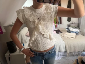 Vit spetsblus med volanger från Zara - Supersöt vit blus från Zara i storlek S, med volanger och spets framtill och på axlarna. Blusen har korta ärmar och är stickad med ett snyggt mönster. Har prislappen kvar!