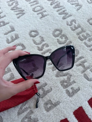 Svarta cat eye solglasögon Chanel - Snygga svarta solglasögon från Chanel med cat eye-form och mörka tonade glas. Ramen är i blank svart plast och loggan syns diskret i hörnet. Perfekt accessoar för en trendig look.