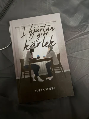 I hjärtan gror kärlek - En bok med ett modernt och mysigt omslag där två personer samtalar över en kopp te. Perfekt för dig som gillar berättelser om relationer, känslor och vardagsliv. Passar unga vuxna som söker en varm och relaterbar läsupplevelse.