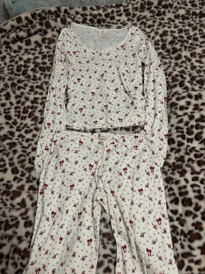 Vit blommigt sett från Nelly - Supersöt vit blommigt sett från Nelly med små röda blommor och rosetter över hela tyget. Byxorna har normal passform, dragsko i midjan och är gjorda i mjukt bomullsmaterial. Perfekta för chill dagar hemma eller mysiga kvällar.