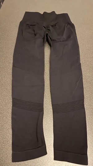 Svarta seamless leggings - Svarta leggings med hög midja och ribbade detaljer längs benen. De är tillverkade i ett stretchigt syntetmaterial som sitter tight och bekvämt. Perfekta för träning eller chill, med en clean och sportig look.