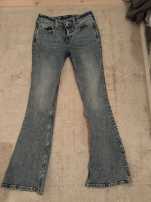 Blå low-rise flare jeans från Hollister - Snygga blå jeans från Hollister med klassisk stretch och low-rise flare passform. Modellen har utsvängda ben, fickor och slitna detaljer för en cool vintagekänsla. Väldigt fin jeans tvätt färg!