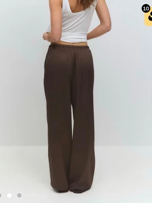 Bruna satinbyxor - Snygga bruna linnebyxor med vid passform och elastisk midja. Byxorna har en lätt glansig satinlook och faller snyggt längs benen. Perfekta att styla med crop top eller oversized kavaj för en trendig look.