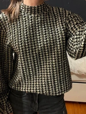 Svartvit stickad tröja med hundtandsmönstrad  - Säljer en svartvit stickad tröja med klassiskt hundtandsmönster. Tröjan har rak passform, hög hals och långa ärmar. Perfekt för dig som gillar retrostil och vill ha något som sticker ut i garderoben.