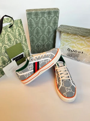 Gucci sneakers med GG-mönster - Snygga sneakers från Gucci i grått tyg med vitt GG-mönster och klassiska gröna och röda ränder på sidan. Skorna har vita snören, orange detalj runt sulan och grön insida. Perfekta för dig som vill sticka ut med lyxig streetstyle.