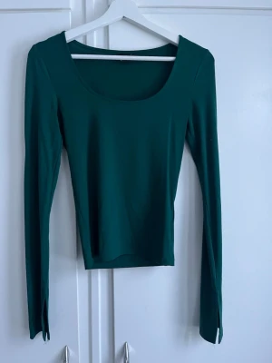 Mörkgrön långärmad topp - En stilren mörkgrön topp med lång ärm och bred, rundad urringning. Toppen har en tight passform och är tillverkad i ett mjukt, stretchigt material som sitter snyggt på kroppen. Perfekt att matcha med både jeans och kjol.
