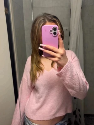 Ljusrosa stickad tröja med v-ringning - Superfin ljusrosa stickad tröja med v-ringad hals och avslappnad passform. Tröjan har långa ärmar och är gjord i ett mjukt, fluffigt material som känns skönt mot huden. Perfekt att styla med jeans eller kjol för en söt look.