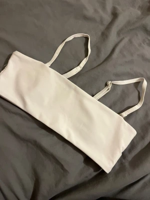 Vit bikini topp - En enkel och stilren vit bikini topp med tunna axelband. Toppen är rak i modellen och har justerbara band för bästa passform. Perfekt att bära under transparenta plagg eller som en minimalistisk topp. Materialet känns mjukt och stretchigt. Passar även xs! 