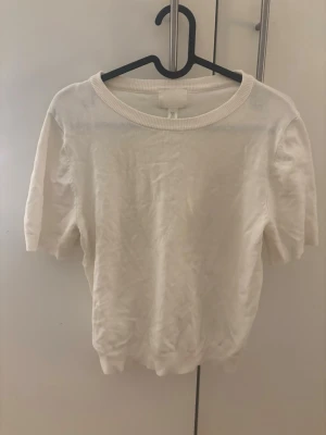 Vit kortärmad topp med rund hals - En stilren vit topp med rund halsringning och korta ärmar. Toppen har en enkel och klassisk design med ribbade kanter vid hals och nederkant. Perfekt att matcha med jeans eller kjol för en clean look.