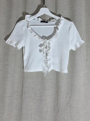 Vit volang topp Shein - En topp från Shein i strI S. Den har volanger både fram och runt nacken. Den har även volang på ärmarna. Knytning fram och ribbat mönster. Den är i fint skick utan fläckar eller liknande. Det ända är att den är lite nopprig. Katt finns i hemmet