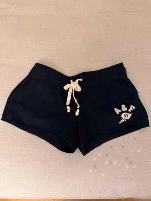 Mörkblå shorts från Abercrombie & Fitch - Mörkblå shorts från Abercrombie & Fitch med vit snörning i midjan och broderad logga på ena benet. Mjukt material och sportig passform, perfekta för sommardagar eller chill hemma.