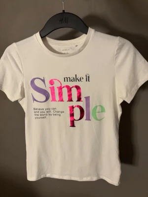 Vit t-shirt med färgat tryck -  Vit t-shirt med färgat tryck, oanvänd. Vet inte vart den vart den är ifrån.