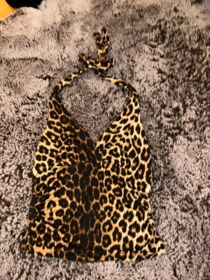 Leopardmönstrad halterneck topp - Snygg leopardmönstrad halterneck topp med knyt i nacken. Perfekt för dig som vill sticka ut och addera lite edge till din outfit. Mjuk och stretchig känsla, figurnära passform och djup v-ringning framtill.