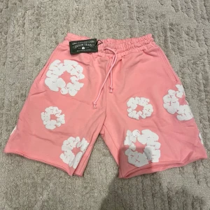 Rosa shorts med vita blommor - Snygga rosa shorts från Leisure Team med vita blommönster och elastisk midja med snörning. Perfekta för sommardagar och avslappnade tillfällen. Mjukt material och avslappnad passform.