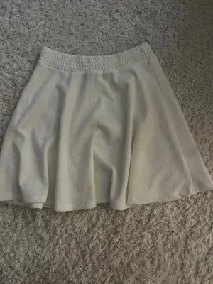 Vit kortkjol med resårmidja - Enkel och stilren vit kortkjol med bred resår i midjan. Kjolen har en lätt utsvängd form och är tillverkad i ett mjukt tyg som ger ett snyggt fall. Som ny använt två gånger då den inte passar💓