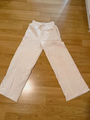 Vita mjukisbyxor med snörning - Vita mjukisbyxor med breda ben och dragsko i midjan. Sköna och avslappnade, perfekta för chill dagar hemma eller när du vill ha en casual look. Tillverkade i mjukt material som känns bekvämt mot huden.