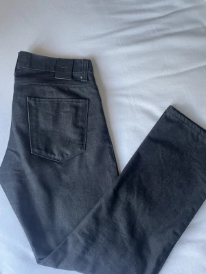 Svarta jeans från Riley - Snygga svarta jeans med klassisk femficksdesign och raka ben. Jeansen har en stilren look utan synliga loggor och är perfekta för dig som gillar en enkel och clean stil. Tillverkade i ett slitstarkt jeanstyg som passar till det mesta.