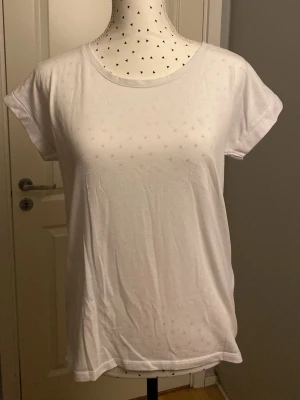 Vit basic t-shirt i bomull - Enkel vit t-shirt med rund hals och korta ärmar. Tillverkad i mjuk bomull och har en avslappnad passform. Perfekt att matcha med jeans eller shorts för en clean och stilren look. Lite nopprig.