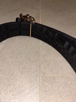 Burberry bälte med guldspänne - Snyggt bälte från Burberry med klassiskt rutmönster i beige, svart och rött. Bältet har ett stilrent guldspänne med ett B framtill. Perfekt accessoar för att lyfta din outfit.