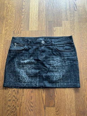 Svart leopardmönstrad jeanskjol ONLY - Cool svart jeanskjol från ONLY med diskret leopardmönster och slitna detaljer. Kjolen har klassiska fem fickor, bälteshällor och dragkedja fram. Perfekt för dig som vill ha en edgy och trendig look.