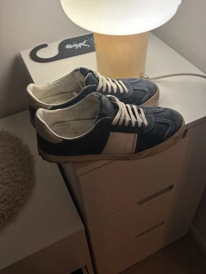 Valentino Garavani sneakers blå/vit - Snygga sneakers från Valentino Garavani i mörkblå mocka med vita detaljer och snörning. Klassisk rund tå och platt sula. Perfekta för dig som gillar stilrena och exklusiva sneakers med en sportig touch.