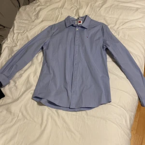Blå skjorta från Tommy Hilfiger - Klassisk ljusblå skjorta från Tommy Hilfiger med diskret logga på bröstet. Skjortan har lång ärm, knappar framtill och är tillverkad i bomull. Perfekt för en clean och stilren look. Den är i L men passar mig perfekt som har M/S