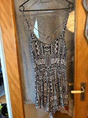 Svartvit kort klänning med mönster - Kort klänning i svartvitt med grafiskt mönster och smala axelband som korsas i ryggen. Klänningen har en avslappnad passform och är perfekt för varma dagar. Tillverkad i mjukt material som känns skönt mot huden.