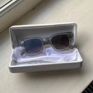 Transparenta solglasögon med lila ton - Snygga solglasögon med transparent båge och rektangulära glas. Glasen har en lila ton som ger en cool vibe. Kommer med ett vitt fodral. Perfekta för dig som vill sticka ut med en modern och stilren look.