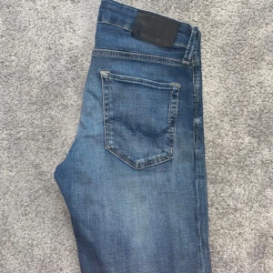 Blå  Jack and jones  jeans slim fit - 28/30 Snygga blå Jack and jones jeans med klassisk femficksdesign och svarta läderpatch bak. Jeansen har en slim passform och är tillverkade i slitstarkt denim. Perfekta för dig som gillar en tidlös och avslappnad stil. 