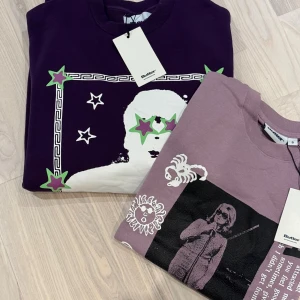 Lila Reggae-tröja från Butter Goods - Cool lila tröja från Butter Goods med stort Reggae-tryck framtill i vitt, grönt och lila. Motivet har stjärnor och grafiska detaljer, samt texten 'Reggae' i grönt. Tröjan har rund hals, långa ärmar och ribbade muddar. Perfekt för dig som gillar streetwear och musik. Säljer både sweetshirt och t- shirt ihop 