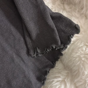 Mörkgrå långärmad tröja med schrunch detaljer nedtill - Superfin, mörkgrå långärmad ribbad tröja med schrunch detaljer nedtill. Tröjan är från märket PompDeLux och är i storlek 38/40 men passar även dig som bär storlek s/xs.💗