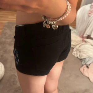 Svarta shorts med blått mönster H&M - Säljer ett par svarta shorts från H&M i storlek 34. De har coola blå och vita geometriska detaljer på sidorna, klassisk knappstängning och fickor både fram och bak. Passformen är tight och midjan är låg, perfekt för dig som gillar en trendig look.