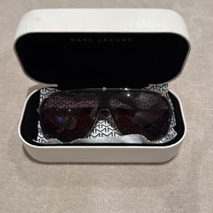 Marc Jacobs pilotbågar solglasögon - Snygga solglasögon från Marc Jacobs med pilotformade bågar i silverfärgad metall och mörka linser. Klassisk och stilren design med diskret logga på skalmen. Kommer med originaletui.