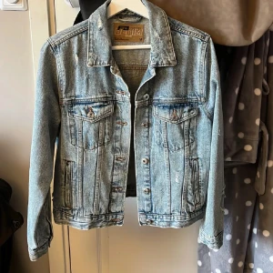 Ljusblå jeansjacka - Snygg ljusblå jeansjacka i klassisk modell med krage, knappar framtill och två bröstfickor med lock. Jackan har slitna detaljer för en cool vibe och är tillverkad i jeansmaterial. Perfekt att slänga över en hoodie eller t-shirt.