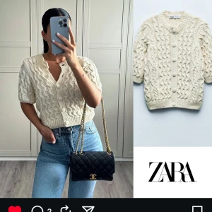 Beige kabelstickad kofta från ZARA - Kabelstickad kofta från ZARA i beige  med korta ärmar och stora tygklädda knappar framtill. Koftan har v-ringning och är gjord i mjuk bomull. Perfekt till jeans eller kjol för en chill och trendig look.
