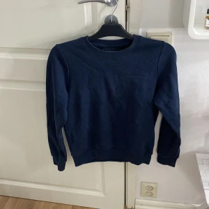 Mörkblå Peak Performance sweatshirt XS - En stilren mörkblå sweatshirt från Peak Performance i storlek XS. Tröjan har rund halsringning, ribbade muddar och diskret broderad logga på bröstet. Perfekt för dig som gillar en enkel och klassisk look.