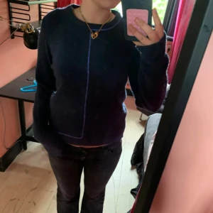 Mörkblå stickad tröja med lila kant - Säljer en mörkblå stickad tröja med lång ärm och en cool lila kant som går längs framsidan och nederkanten. Tröjan har en rund halsringning och är lite loose i passformen, perfekt för dig som gillar chill och enkel stil.