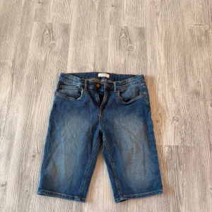 Blå jeansshorts från Lindex Detroit - Säljer ett par klassiska blå jeansshorts från Lindex Detroit med fem fickor, knapp och dragkedja framtill. Shortsen har normal passform och är tillverkade i bomull med snygga sömmar och bälteshällor. 