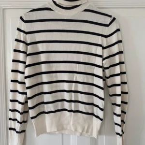 Randig polotröja i bomull - Vit och svart randig polotröja med lång ärm. Tröjan har en klassisk passform och är tillverkad i mjuk bomull, perfekt för lager-på-lager under höst och vår. Enkel att matcha med både jeans och kjol.