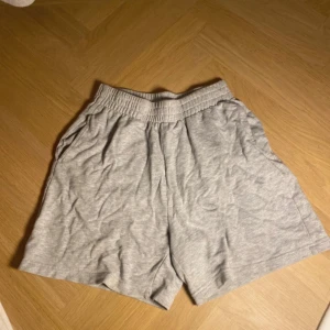 Grå mjuka shorts med resårmidja - Säljer ett par grå shorts med elastisk midja och avslappnad passform. De är tillverkade i mjuk bomull och har fickor på sidorna. Perfekta för chill dagar eller träning.