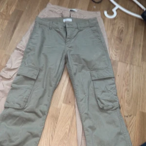 Två par lågmidjade cargobyxor i beige och grön - Säljer två par cargobyxor, ett par i ljusbeige och ett i olivgrönt. Båda har stora sidofickor och klassisk cargomodell. Tillverkade i bomull för skön känsla och avslappnad stil. Perfekta för dig som gillar praktiska och snygga byxor. Slutsålda på ginas sida ock köptes för 500 kr st. Man kan köpa separat för 250 kr st eller båda för 450 🥹🫶🏻 de har sinna små defekter så kom privat ❤️