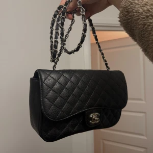 Svart quiltad axelväska - Klassisk svart väska med quiltat mösnter  och silverfärgad kedja med läderdetaljer.